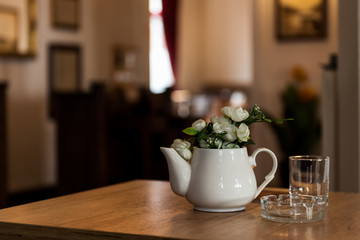 Indoor Restaurant Decoration with Ceramic Milk Pot with Flowers on a Wooden table with a gallery in the background