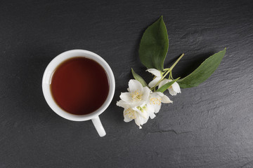 Obraz na płótnie Canvas A cup of tea with jasmine flowers on a dark background. Top view.