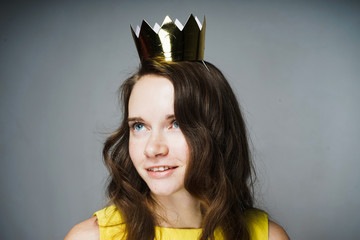 charming young girl in a yellow dress posing, on her head a golden crown, thinking about something...