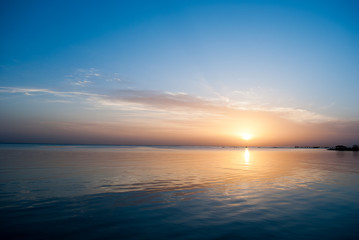 Orange sunrise in blue sky above ocean. Early Morning blue sky with clouds and sun above sea. Sunrise on blue sky and cold water. Water reflex