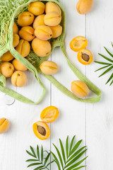 Apricots in a string bag and green leaves on a white board..