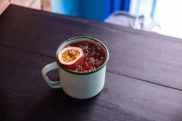 Iced Passion fruit juice served in zinc cup with a cut half of fresh passion fruit.
