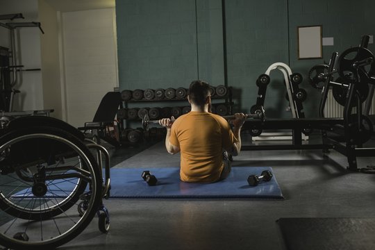 Rear view of handicapped man exercising with barbell in gym