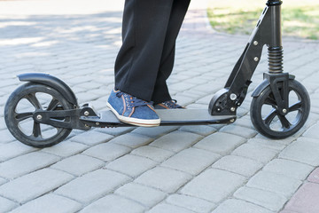 Male legs in trousers and sneakers on a kick scooter, close-up