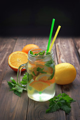 Water with ice, lemon, orange, mint and melissa. Summer cocktail. A refreshing drink. Close-up. The selected focus. The concept of proper nutrition and lifestyle.