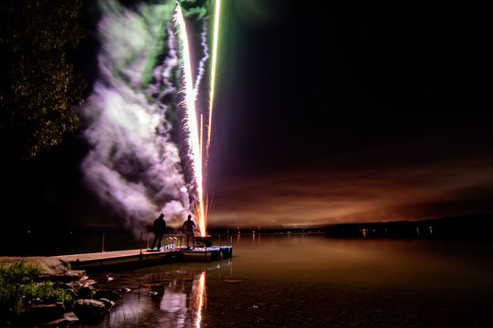 Fireworks on a dock over the water with smoke and lake horizon