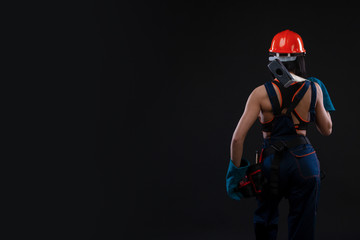 Back view of a female worker holding a hammer and helmet on black background
