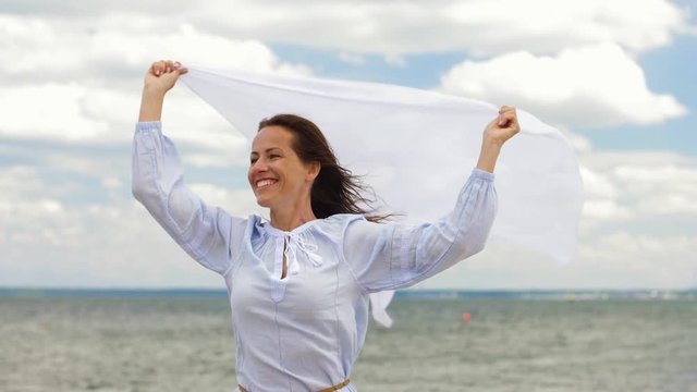 people and leisure concept - happy woman with shawl waving in wind on summer beach