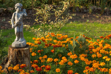 Garden statue on treetrunk between flowers