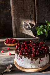 Chocolate cake with whipped cream on wooden desk and wooden background. Cherry cake with chocolate. Raspberry in wooden plate. Rustic foodphotography. Still life food.