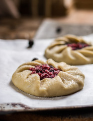 Raw summer galette with berries, raspberry, blueberry, blackberry, apple and crusty sugar vegetarian dough. Summer food, summer pie on parchment paper. Preparation, cooking food, raw dough. Apple pie.