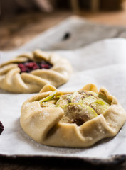 Raw summer galette with berries, raspberry, blueberry, blackberry, apple and crusty sugar vegetarian dough. Summer food, summer pie on parchment paper. Preparation, cooking food, raw dough. Apple pie.