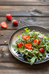 Fresh salad with arugula and strawbery with balsamic sauce and pine nuts. Vegetarian food. Salad with berries. Vitamin food, diet salad on wooden background in black plate.