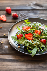 Fresh salad with arugula and strawbery with balsamic sauce and pine nuts. Vegetarian food. Salad with berries. Vitamin food, diet salad on wooden background in black plate.