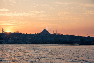 Naklejka premium Cityscape of Istanbul with silhouettes of ancient mosques and minarets at sunset on blur background with ship in front. Panoramic view on the old city. Istanbul sunset. selective focus, unfocus
