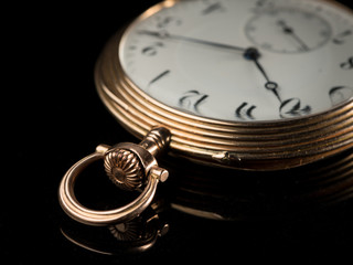 Old golden pocket watch on a black reflective surface