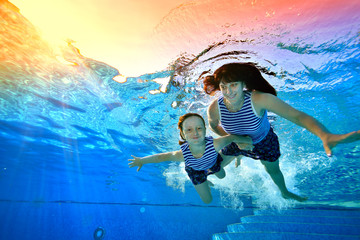 Happy family swimming and playing underwater in the pool. Mom and daughter dive to the bottom of...