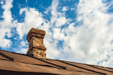 An old brick pipe on the roof of a residential building with an iron roof against a background of...