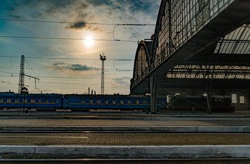 Perspective view of a platform in Lvov Central Railway Station with sunlight cast on trains parking by the platform passengers hurrying for boarding