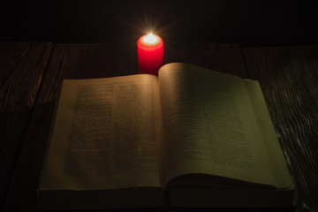 candle and a book of the Bible on wooden background at night