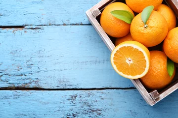 Foto op Plexiglas Orange fruit with green leafs in crate on blue wooden table © 5second