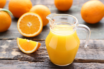 Fototapeta na wymiar Orange fruit with jug of juice on grey wooden table