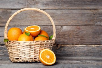 Orange fruit with green leaf in basket on grey wooden table