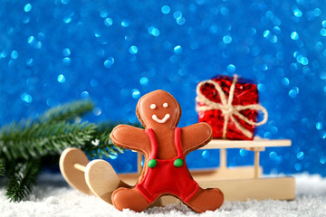 Wooden toy sleigh with gingerbread cookie and gift box on lights background