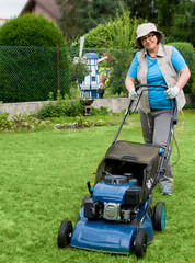 Frau mittleren Alters beim  Rasenmähen in ihrem Garten