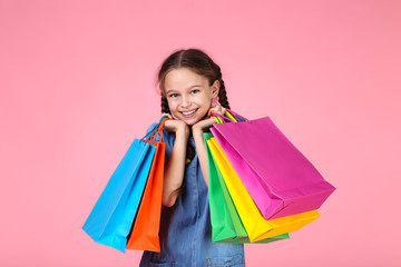 Young girl in denim dress with shopping bags on pink background