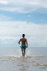 a young man in shorts goes into the water at sea. back view