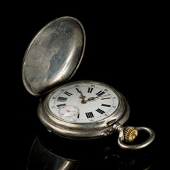 Old pocket watch on a black reflective surface, open lid