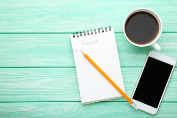 To do list in notepad with smartphone and cup of coffee on wooden table