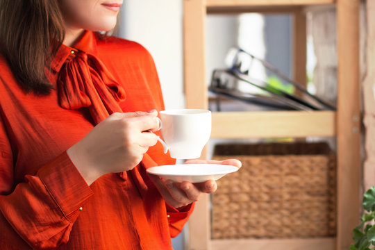 Lady turnt to side with little white cup in her hands. Young businesswoman dressed in bright bold coloured shirt with bow in front having coffee break.