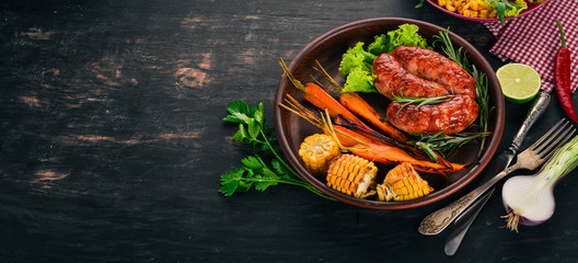 Grilled sausage. Baked Corn and Carrots. On a wooden background. Top view. Copy space.