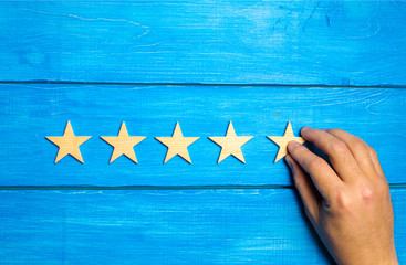 A hand puts the fifth wooden star on a blue background. The critic sets the quality rating. Five stars, the highest quality mark. Raising the rating level of the hotel, restaurant, cafe.