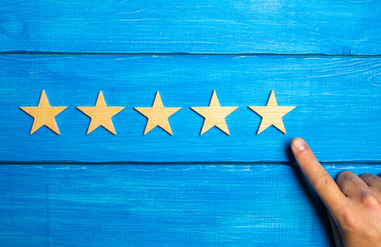 The man's hand points to the fifth star on a blue wooden background. The concept of assessing quality and status. The critic assesses the level of the restaurant, the hotel, the quality of service.