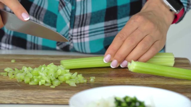 Woman's hands slicing celery on a wooden cutting.