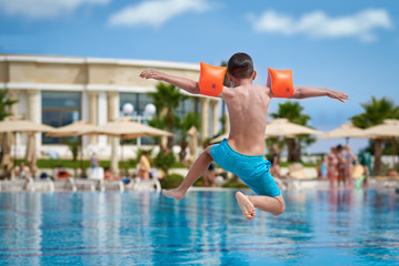 Caucasian boy having fun making fantastic jump into swimming pool at resort. Back view. - 211832601