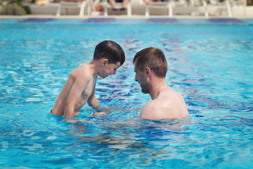 Fototapeta premium Father and son having fun in the swimming pool at the hotel.