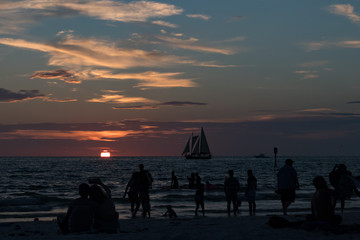 Silhouettes of sailboat on the horizon and people on the beach at sunset