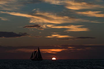 Silhouettes of sailboat on the horizon line at sunset on the beach