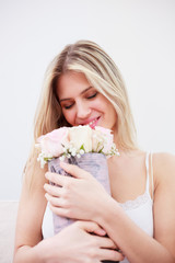 Beautiful happy young woman holding a bouquet of white roses she just received. Relaxing with closed eyes on a sofa in pajamas in a brightly lit room.