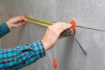 A young working man in a shirt measures with a measuring tape a warmed wall