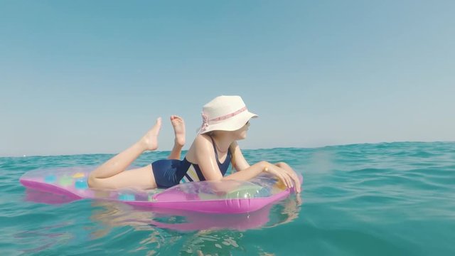 A girl in a hat and sunglasses floats in the sea on an inflatable mattress. Merry vacation concept
