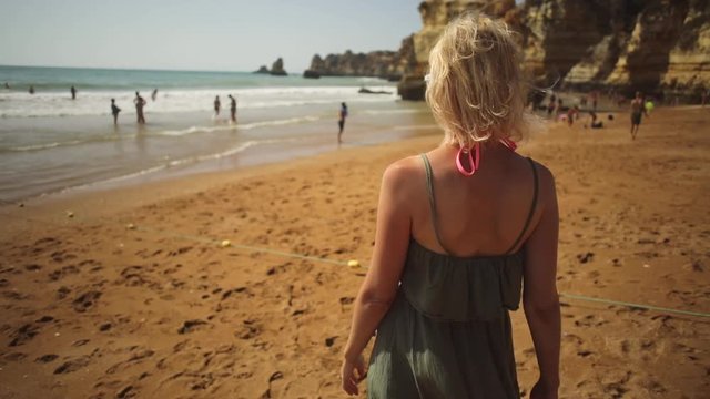 Blonde lifestyle female tourist following on Praia Dona Ana at sunset. Caucasian woman enjoying at popular Dona Ana Beach in Lagos, Algarve coast. Summer holidays in Europe. Tourism in Portugal
