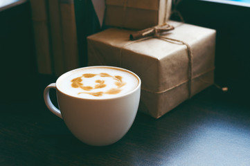 Cappuccino latte art coffee on the table with blur gifts background, vintage blue tone, festive soft mood