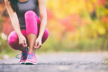 Runner tying running shoes laces in autumn background. Athlete woman getting ready to run race in...
