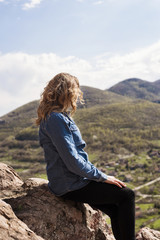 A hiking girl sits on the edge of the cliff and looking at the  valley and mountains