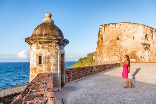 Old San Juan city tourist taking photo in Puerto Rico. Woman using phone taking pictures of ruins of watch tower of San Cristobal Castillo Fort, with ocean background.